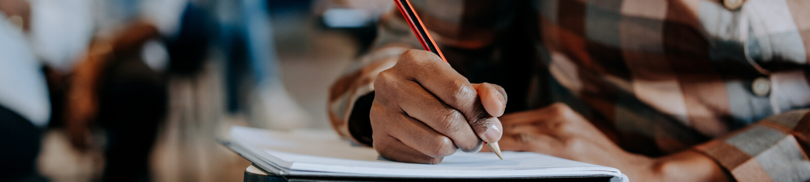 close-up of a hand holding a pencil and writing in a paper notebook