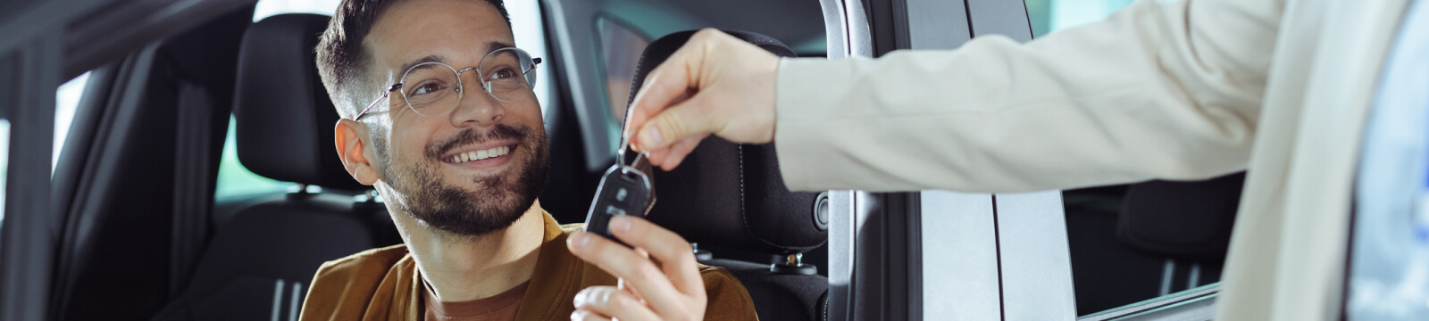 young man sitting in a car and taking the keys from someone out of frame